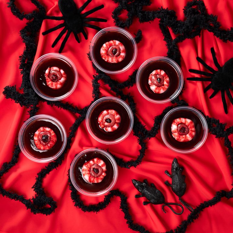 Rum and coke jello shots with eyeballs spread on a red table cloth with plastic spiders and rats.