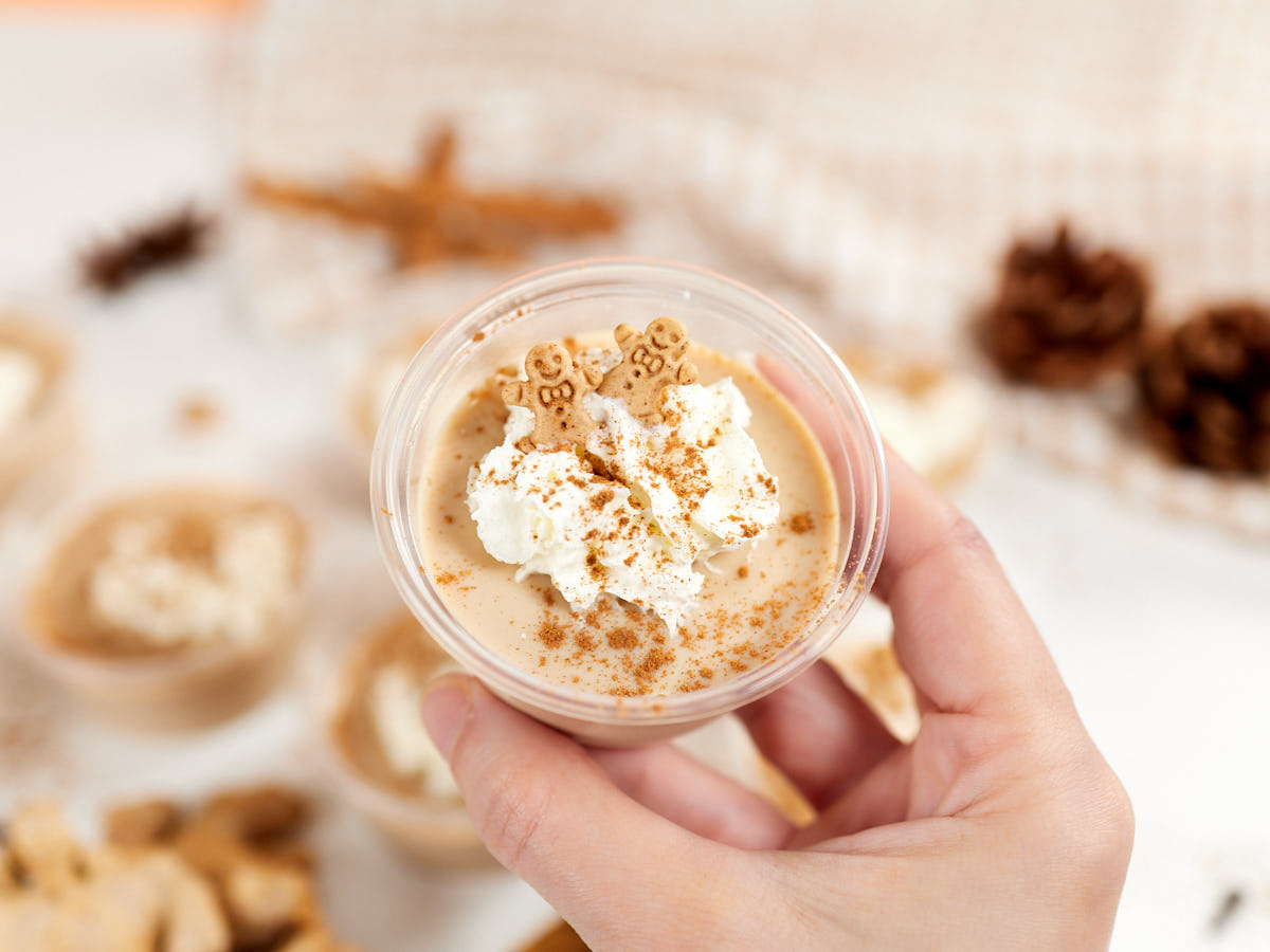 A plastic jello shot cup with gingerbread jello with sprinkles in hand.